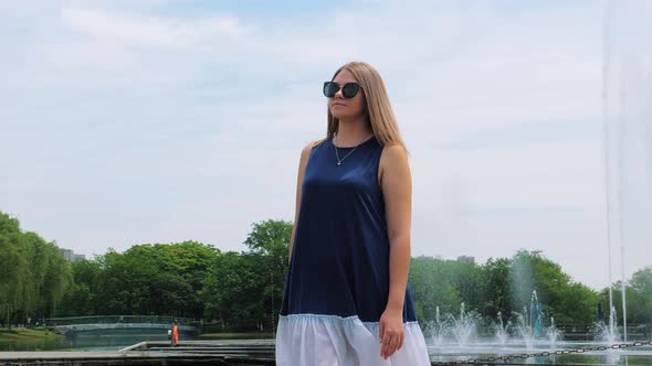 Steadicam Shot of a Beautiful Young Girl in Sunglasses in the Park Near the Fountain