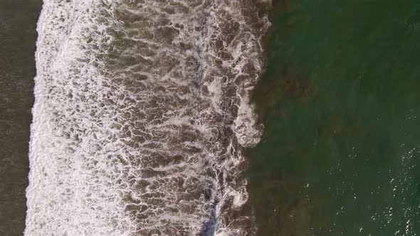 Ocean waves gently rolling onto a tropical beach shoreline in Costa Rica. Aerial top down view