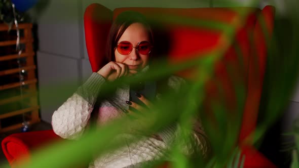 Woman in Stylish Sunglasses Sitting in Armchair with Smartphone