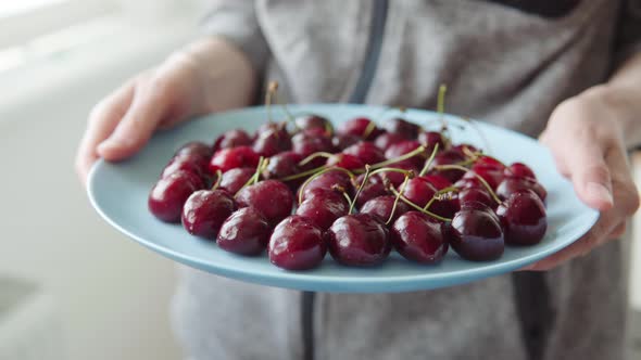 Ripe Fragrant Cherries on a Blue Plate in the Hands of a Woman Closeup