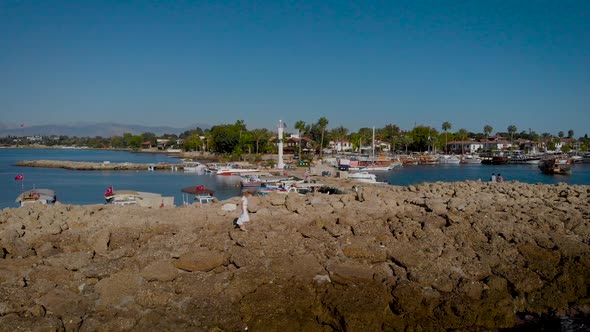 Slender Woman in White Dress Walks on the Stone Bank. Summer Day on the Mediterranean Coast.