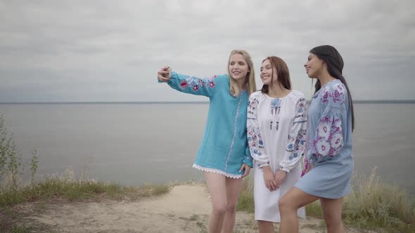 Three Girlfriends Wearing Long Summer Fashion Dress Making Selfies on the Background of a Lake