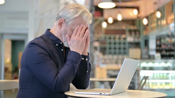 Old Man with Headache in Cafe Using Laptop