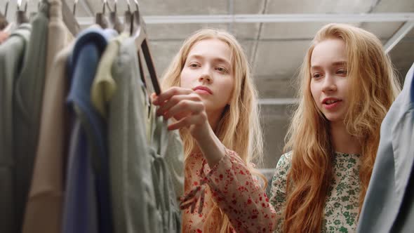 Two Young Beautiful Twin Sisters Choose a Dress in a Boutique