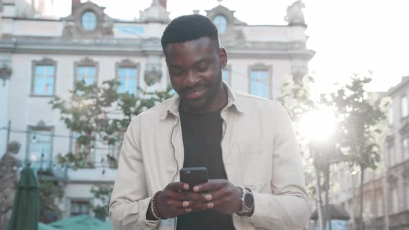 Relaxing walk of Young Attractive Afro American on autumn sunny day with Smartphone.