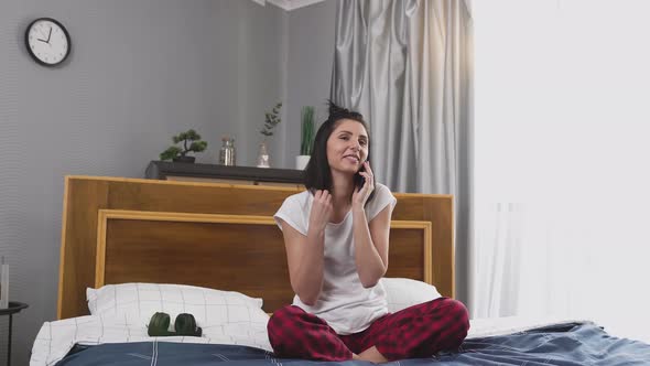 smiling happy young woman in sleepwear talking on phone in contemporary bedroom