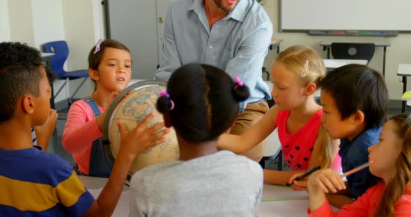 Caucasian male teacher teaching his kids about globe in classroom 4k