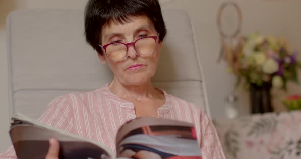 Woman of Retirement Age Reads a Magazine While Sitting in Cozy Armchair at Home