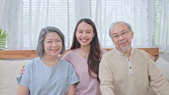 Portrait of Asian happy family staying at home, sitting on sofa in living room and look at camera.