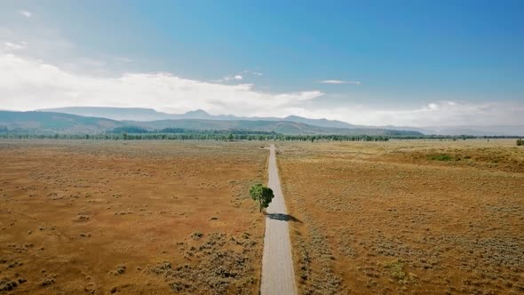 Drone flies over a long road that runs across prairie to the horizon near Mormon Row, Wyoming, USA