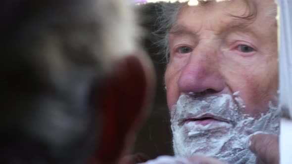 The Curly Old Man is Shaving He is Holding a Mirror in His Hand