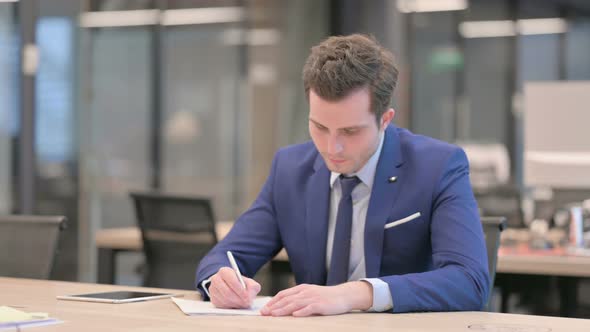 Businessman Writing on Paper in Office