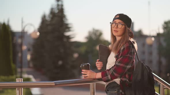 Happy Young Female Student Dressed in Casual Clothing with Cup of Coffee and Backpack Behind Her
