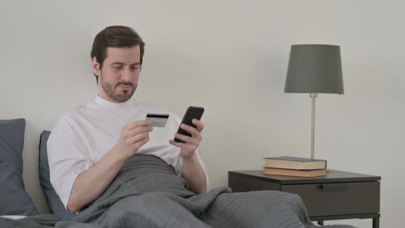 Young Man Making Online Payment on Smartphone in Bed