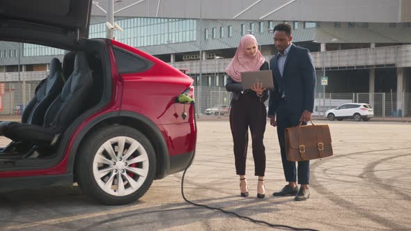 Muslim Woman in Hijab Holding Wireless Laptop and Showing Something to African