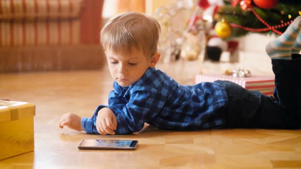 Video of Cute Little Boy Lying on Floor Next To Christmas Tree and Watching Cartoons on Smartphone