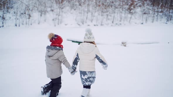 Back view of two children are walking together in the snowy forest. alt