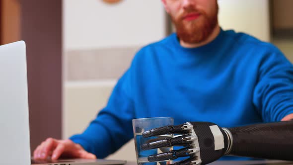 Young Freelance Businessman with Prosthesis Hand Working at Home in Laptop and Drinking Water or Tea