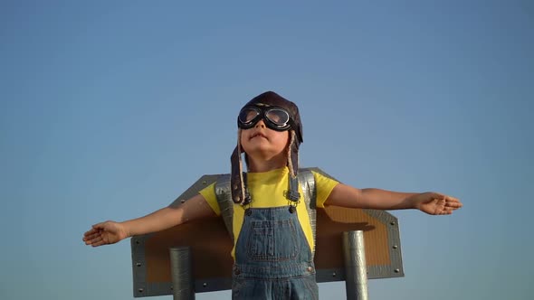 Kid having fun with toy paper wings against summer sky background