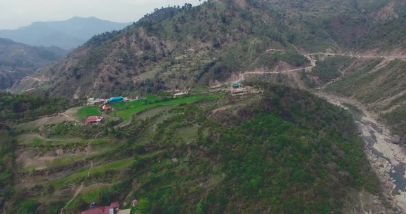 A river between the mountains, houses and a road with the river. A green hills view from drone.