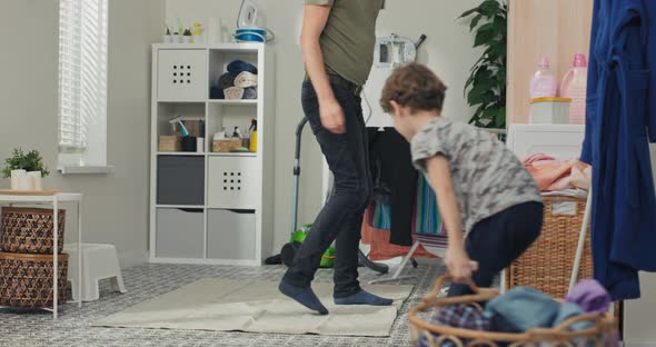 A Dad Walks Into the Laundry Room with His Son Pulling in a Wicker Basket of Clothes