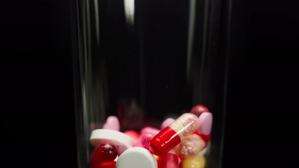 Closeup of Falling Coloured Medicine Tablets Into Glass on Black Background Shooting of Fallen Red