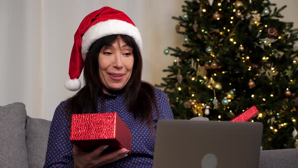 Woman in Santa Claus Hat Opens Gift Box and Surprised Online Video Call Laptop