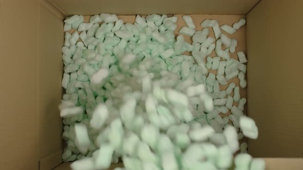 Storyfoam Packing peanuts being poured falling into cardboard box, care shipping products