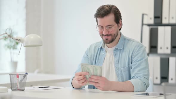 Happy Young Man Counting Dollars at Work