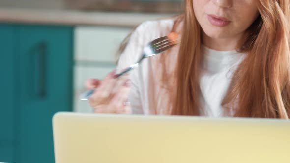 Close-up Cute woman with red hair works in the morning with a laptop in kitchen