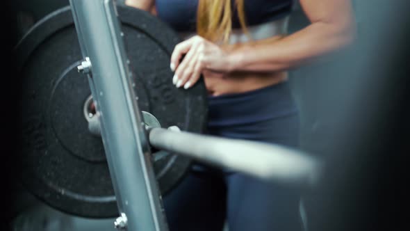 Female bodybuilder putting weight plate on barbell in gym