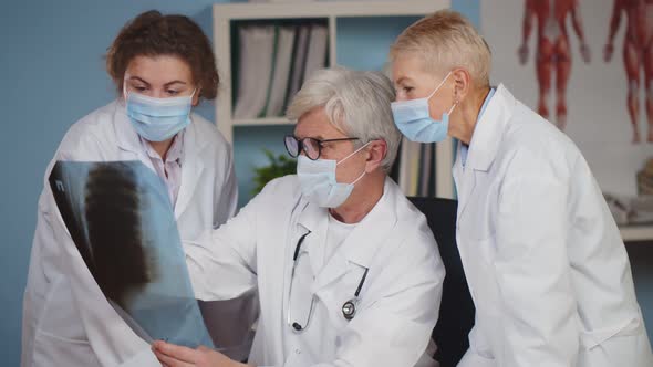 Three Doctors in Safety Mask and Lab Coat Examining Patient Chest X-ray Film