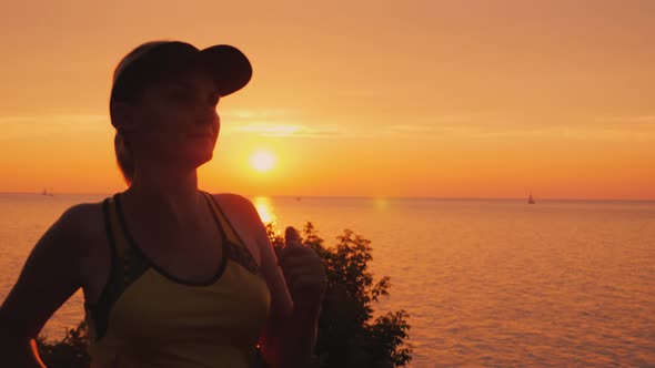 A Young Woman Runs in a Picturesque Place By the Sea Where the Sun Sets Over the Water