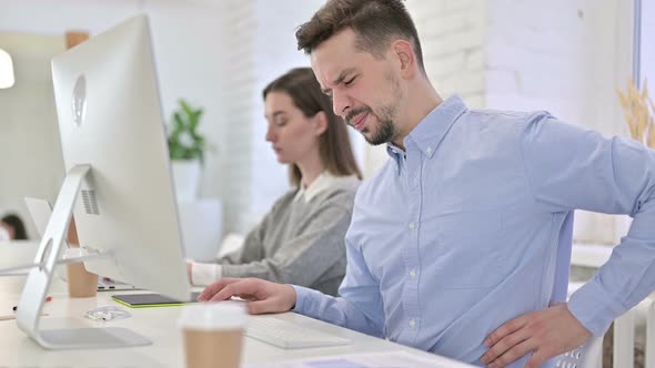 Tired Creative Man Having Back Pain in Modern Office