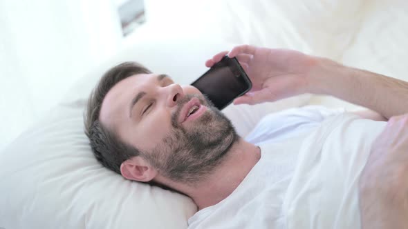 Cheerful Beard Young Man Designer Talking on Smartphone in Bed