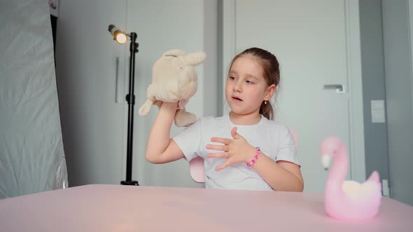 A girl in a home studio looks at the camera and shows a soft toy dog. Child blogger vlogger concept