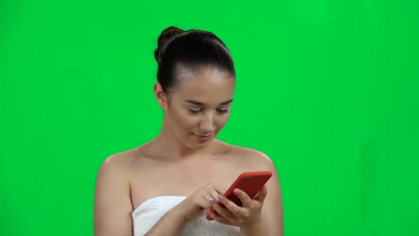 Brunette Girl in a Towel Looks Through Information on the Mobile Phone, Then Speaks By Phone. Green