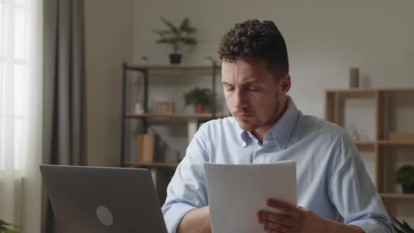 Serious Young Man Read Contract Papers Learn Formal Document Sit at Workplace Desk in Modern Office