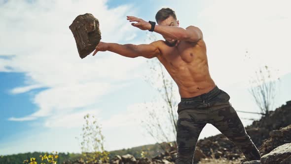 Angry sportsman with muscular body throws stones in nature