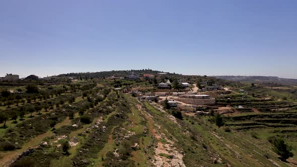 Aerial shot of a small village on the side of a green hill in the mountains, beautiful sunny day, sh