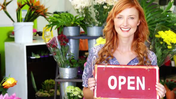 Smiling florist holding open sign on slate in flower shop