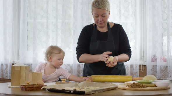 Little Cute Baby Granddaughter Helps Granny Cook Dough for Pastry. Cozy Interior