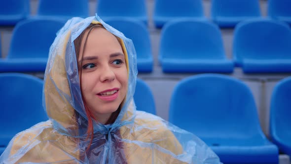 Young Woman in Raincoat Sitting on Stadium Bleachers Alone in Rainy Weather