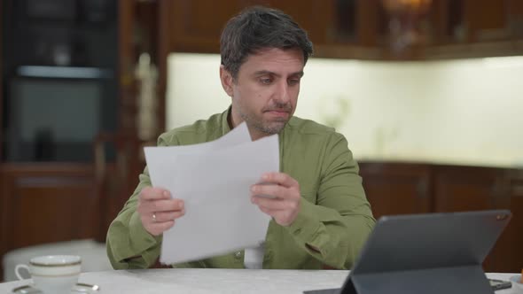 Unshaved Confident Professional Caucasian Man Analyzing Paperwork and Emarket on Remote Working at