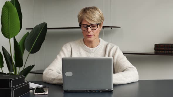 Confident Middleaged Woman Working at a Laptop in a Modern Office Looks Into the Camera