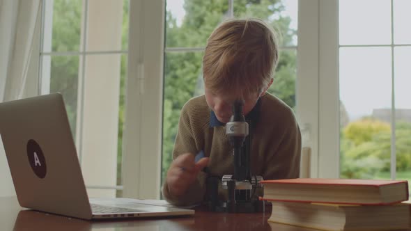 Young Boy Looking at Microscope and Talking to Laptop Studying Online From Home