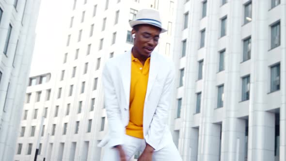 Stylish black guy in chameleon glasses and hat listens to music in wireless headphones