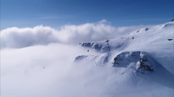 Aerial view over snowy mountain ridge valley with gondola on the cliff in winter