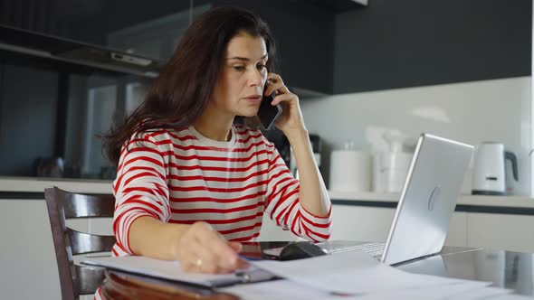 Woman Talking on Phone and Checking Papers in Home Office
