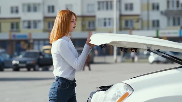 Young stressed woman driver near broken car with popped hood having a prbreakdown